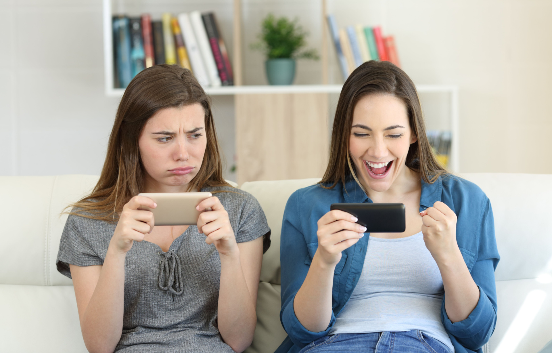 one girl looking envious at the delighted girl next to her on the sofa