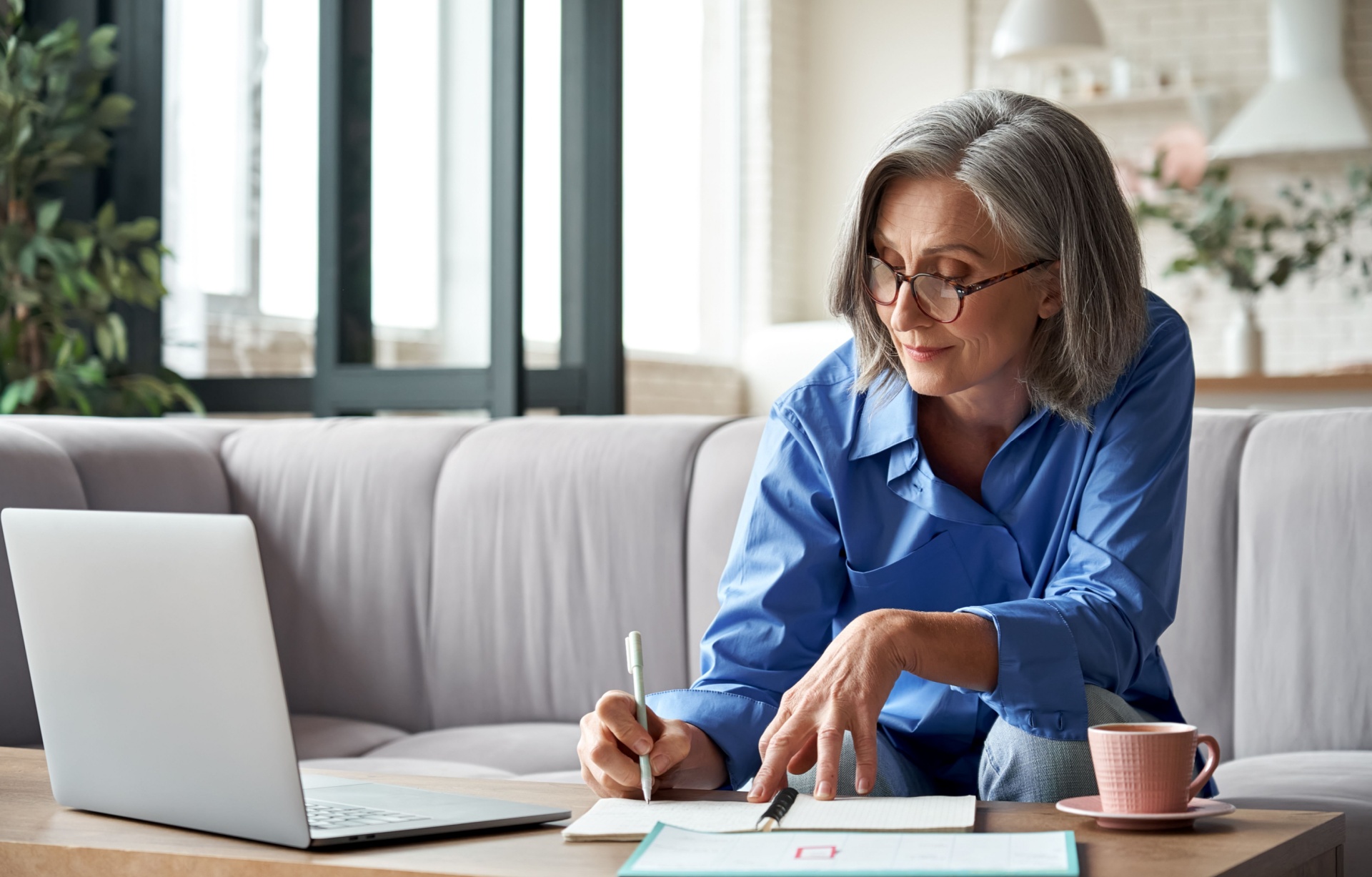 A woman using a laptop and writing notes.